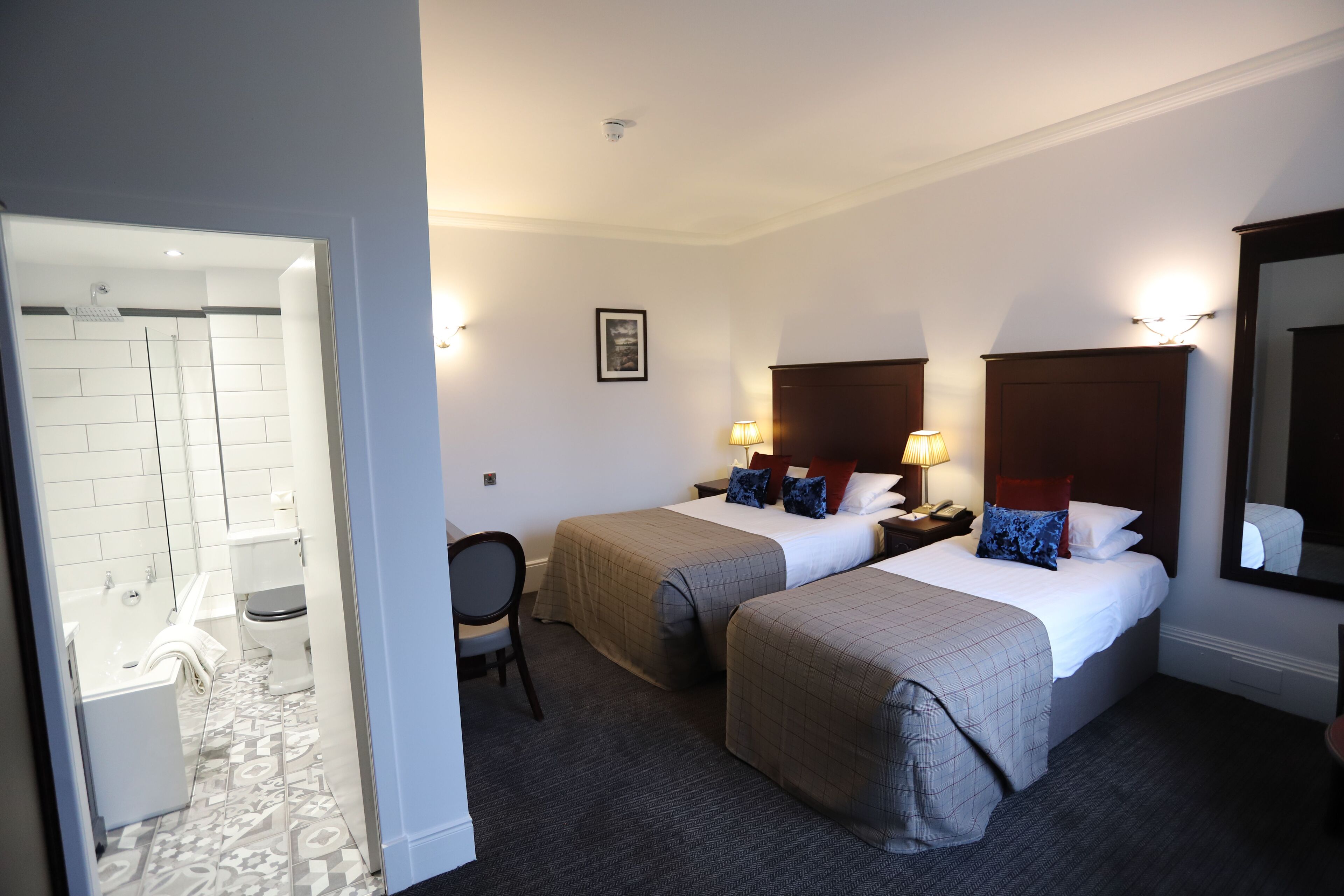 A hotel room with two beds, a bathroom, and a mirror.