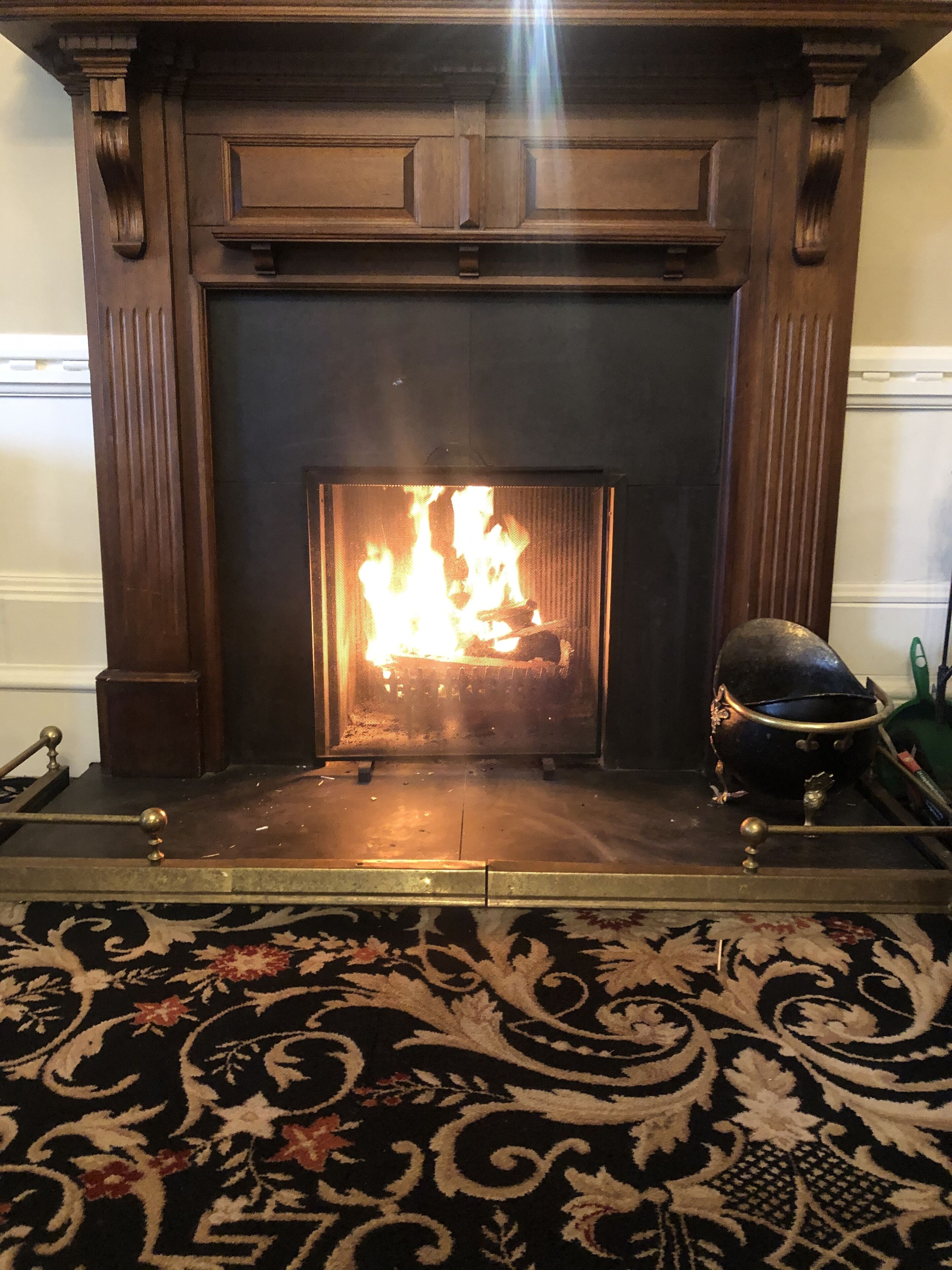 Une cheminée avec un feu, un plateau en métal et un bol décoratif en métal posé sur le manteau de la cheminée.