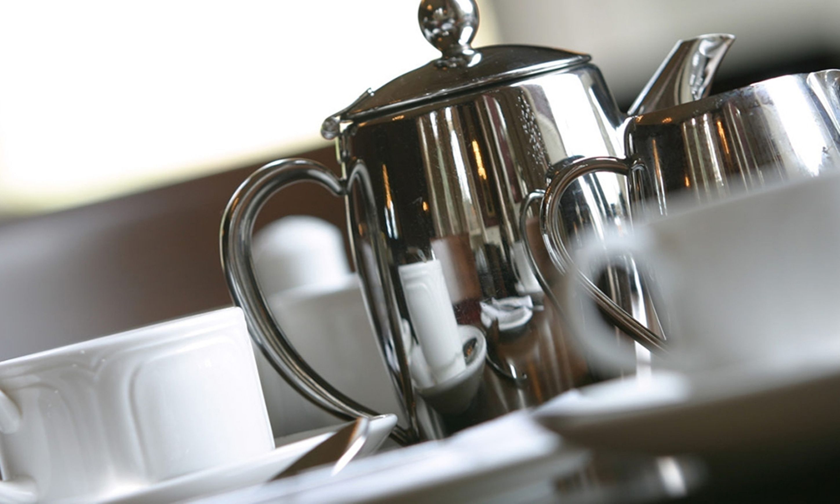 Primer plano de un juego de tetera y cafetera de acero inoxidable sobre una mesa.