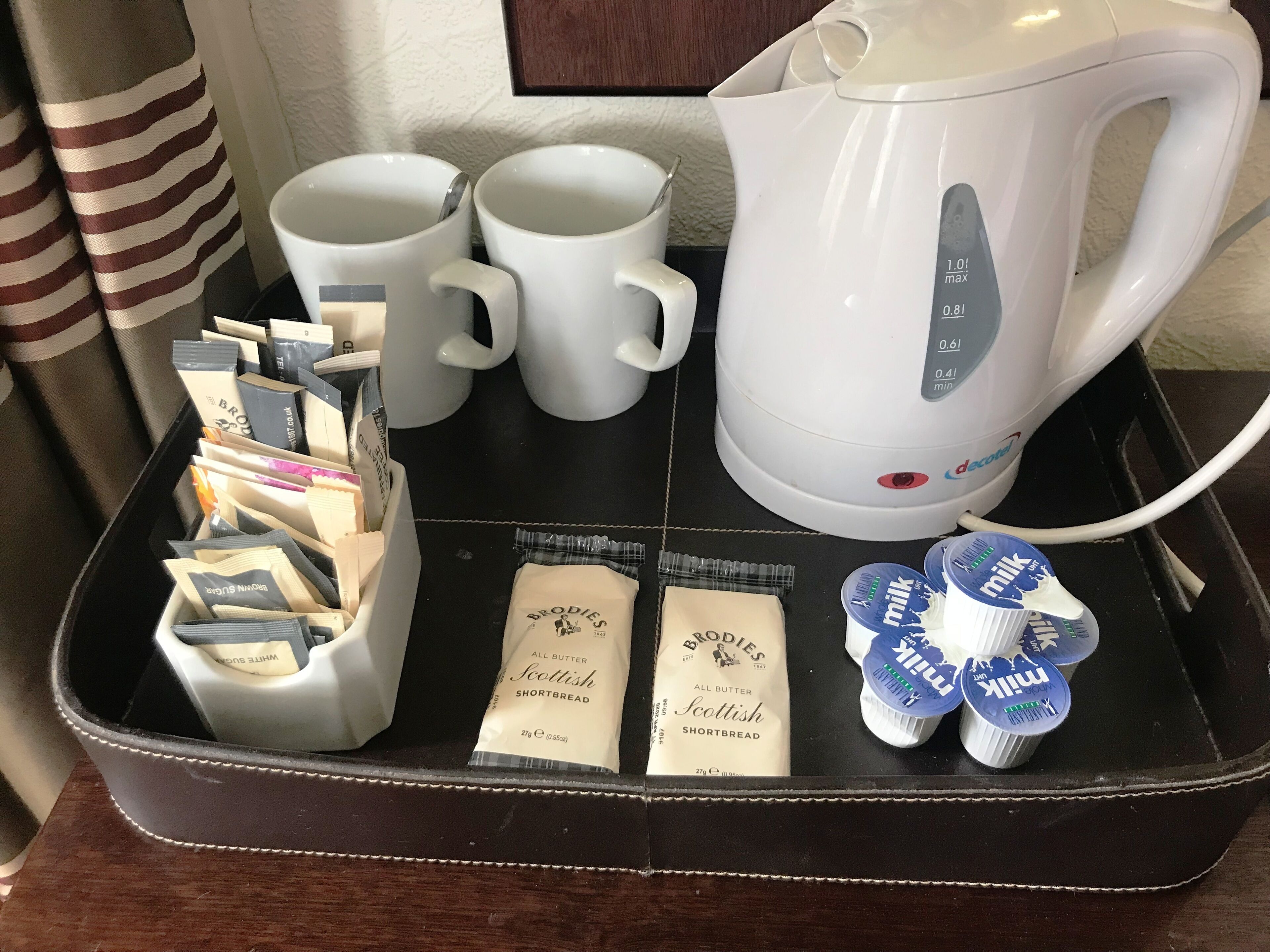A tray with a coffee maker, two white mugs, a tea kettle, and packets of Scottish shortbread and milk.