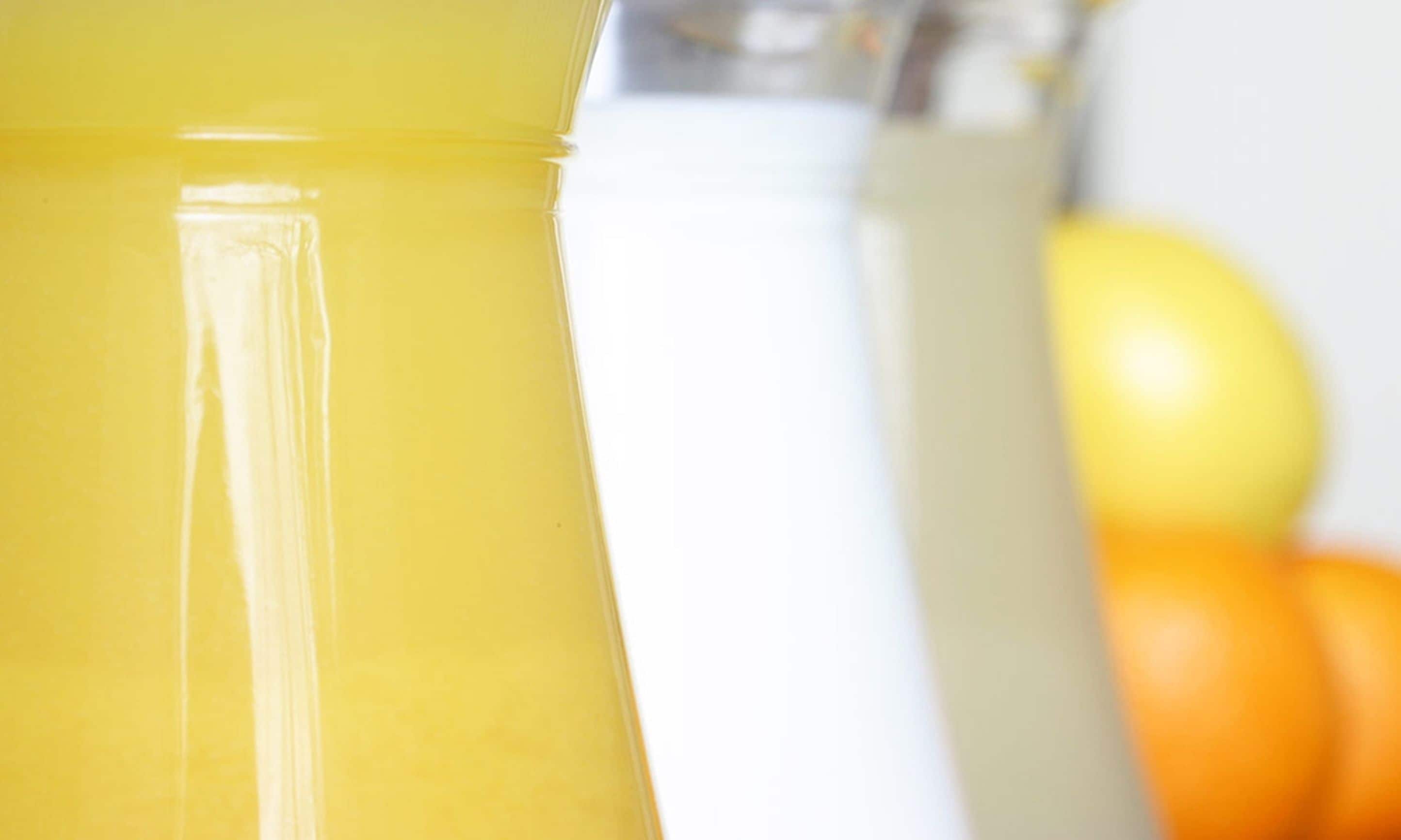 A close-up of a yellow beverage container with a clear liquid, possibly a juice or smoothie, and a white container in the background.