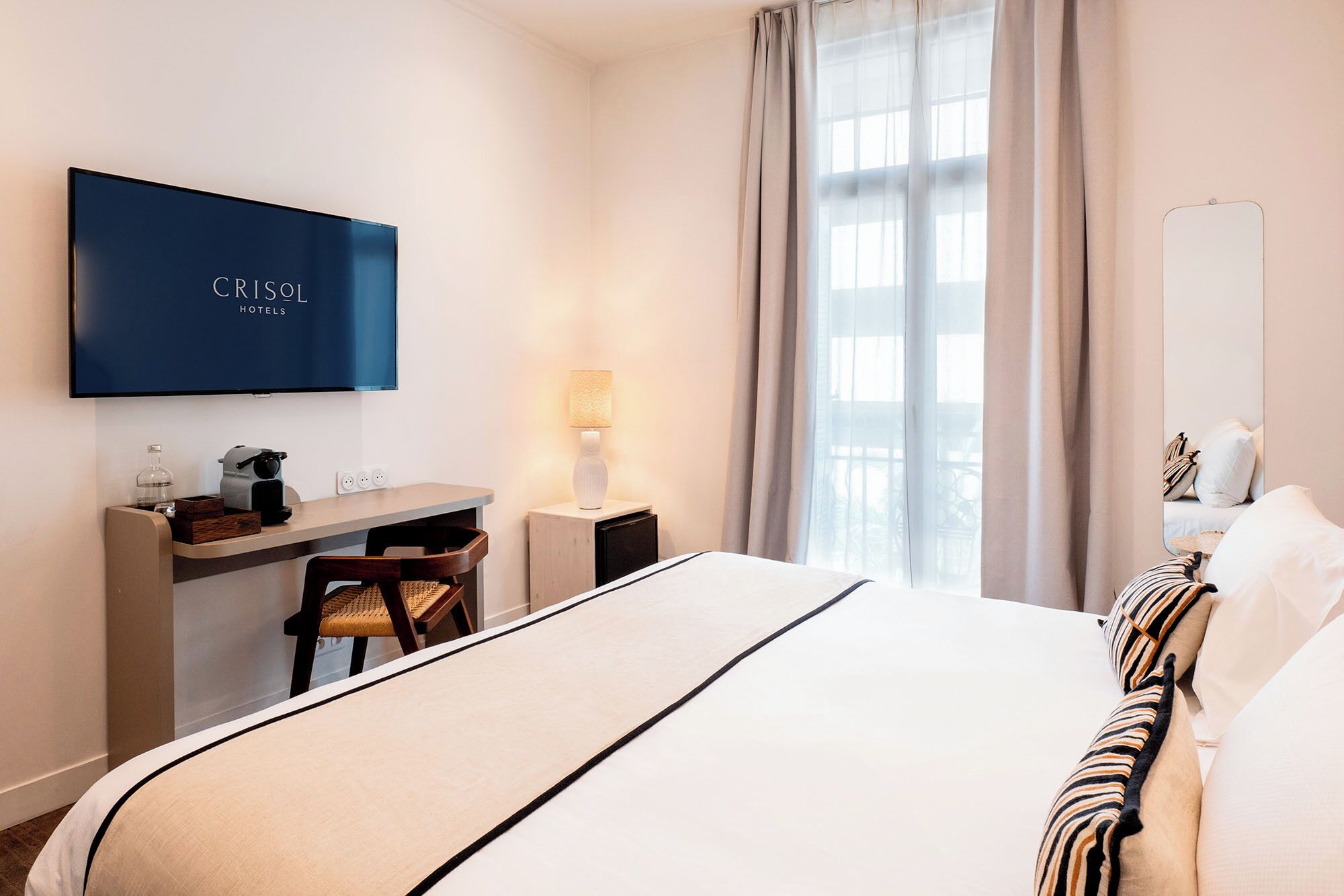 A hotel room with a bed, a desk, a TV, and a window with curtains.