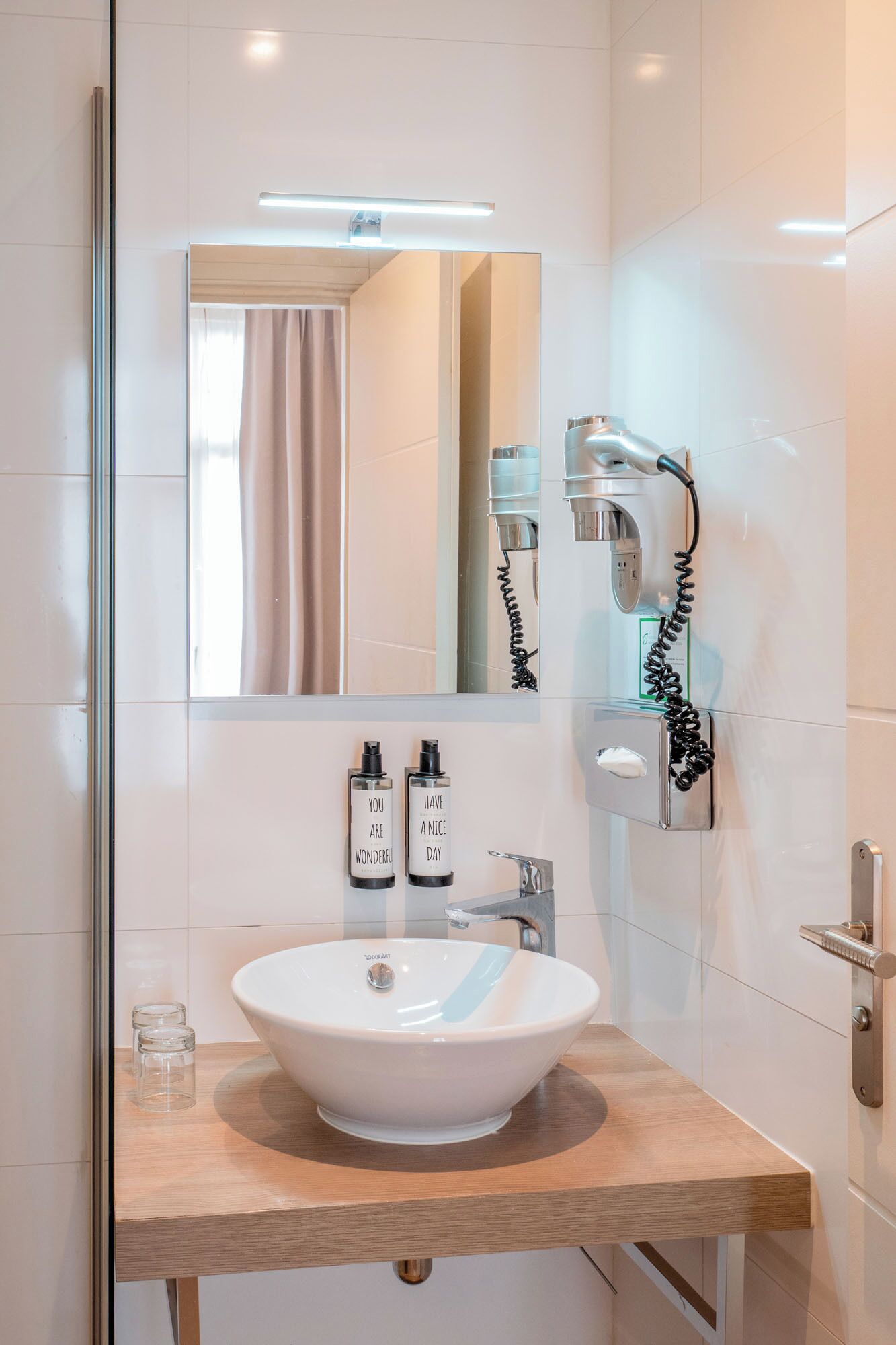 A modern bathroom with a white sink, a mirror, a handheld showerhead, and a towel rack.