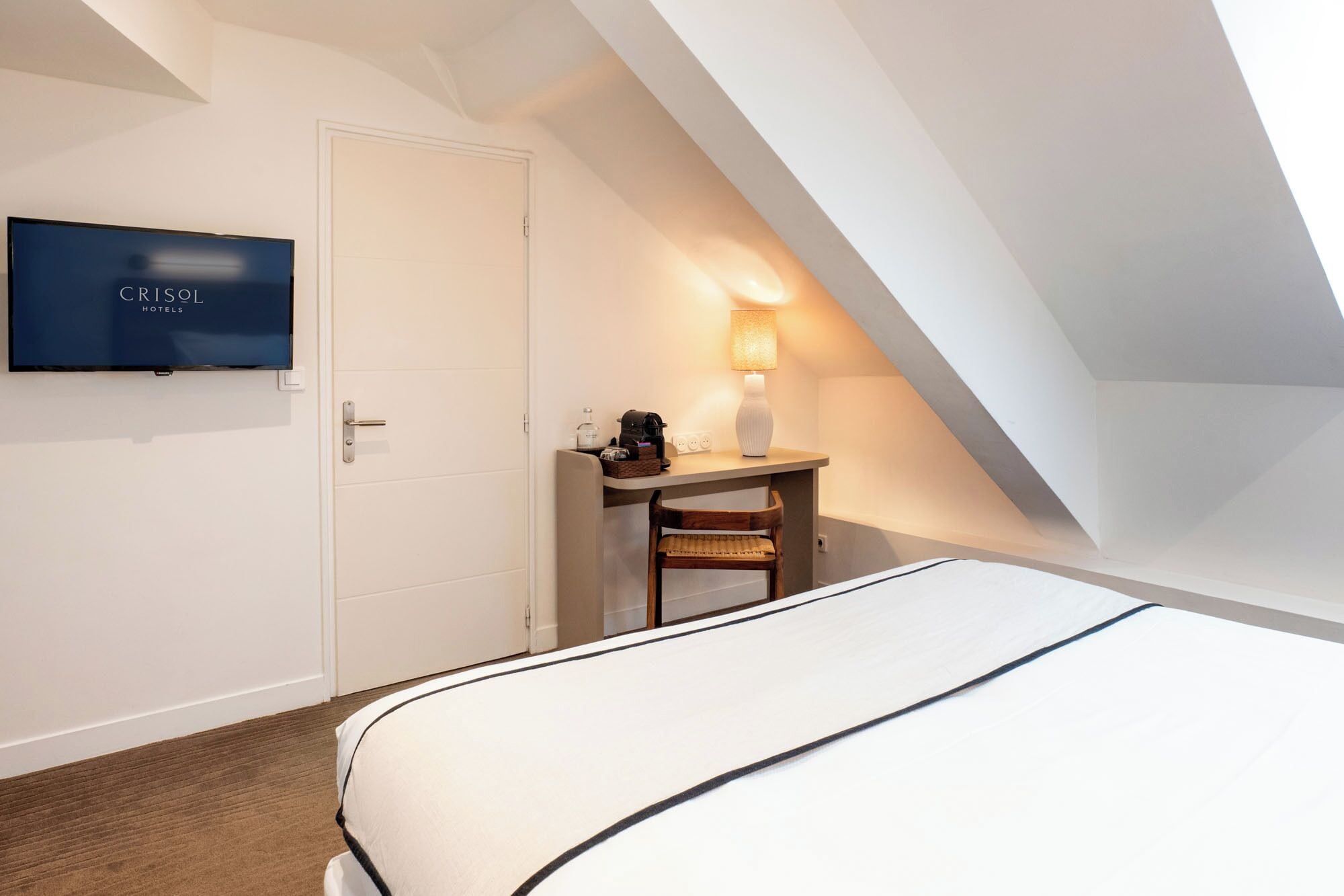 Una habitación de hotel con cama, escritorio con lámpara, televisión y puerta.