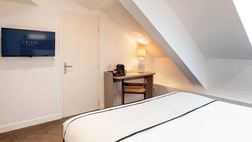 Una habitación de hotel con cama, escritorio con lámpara, televisión y puerta.