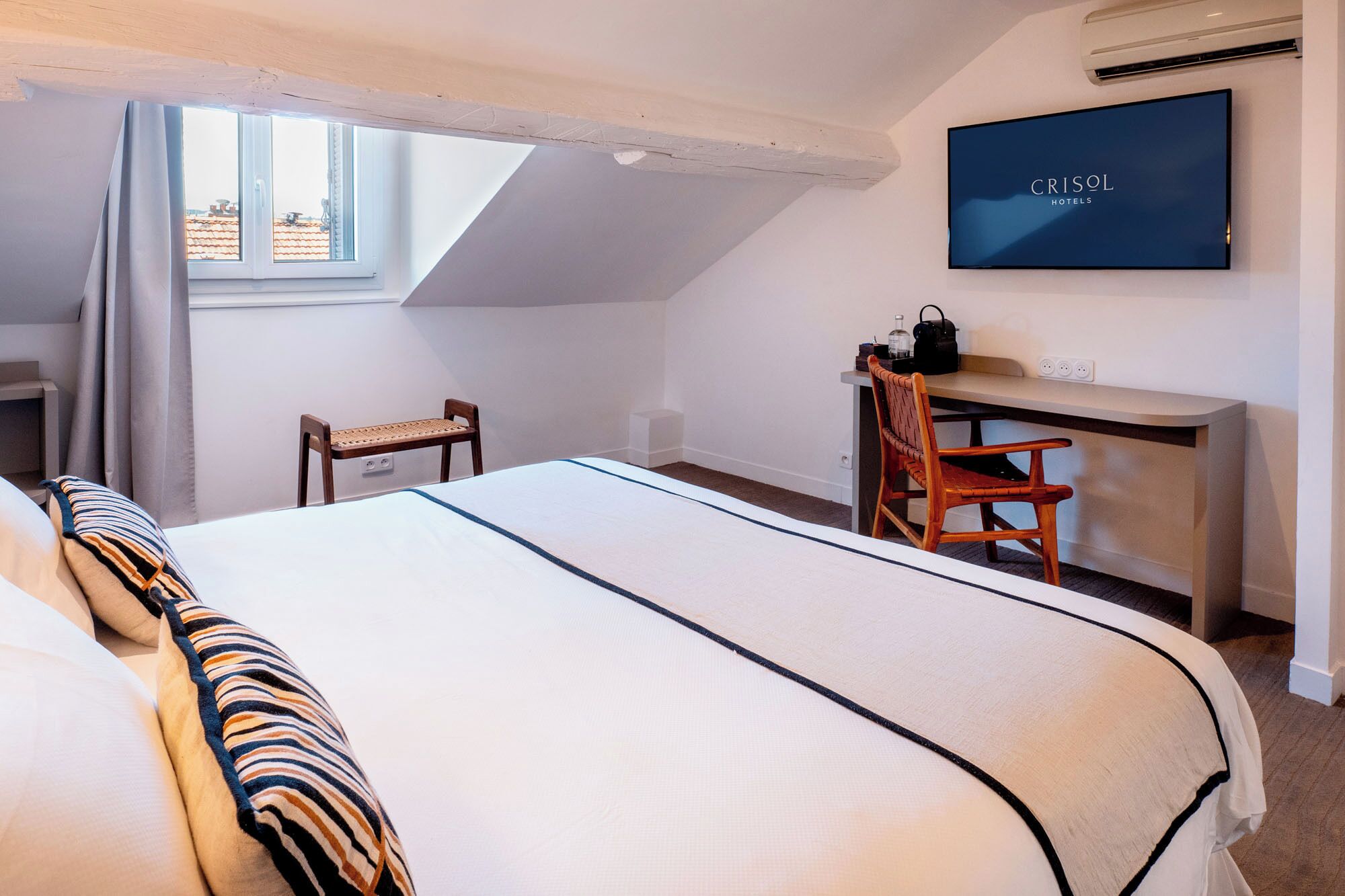 A bedroom with a bed, a desk, a chair, a TV, and a window.