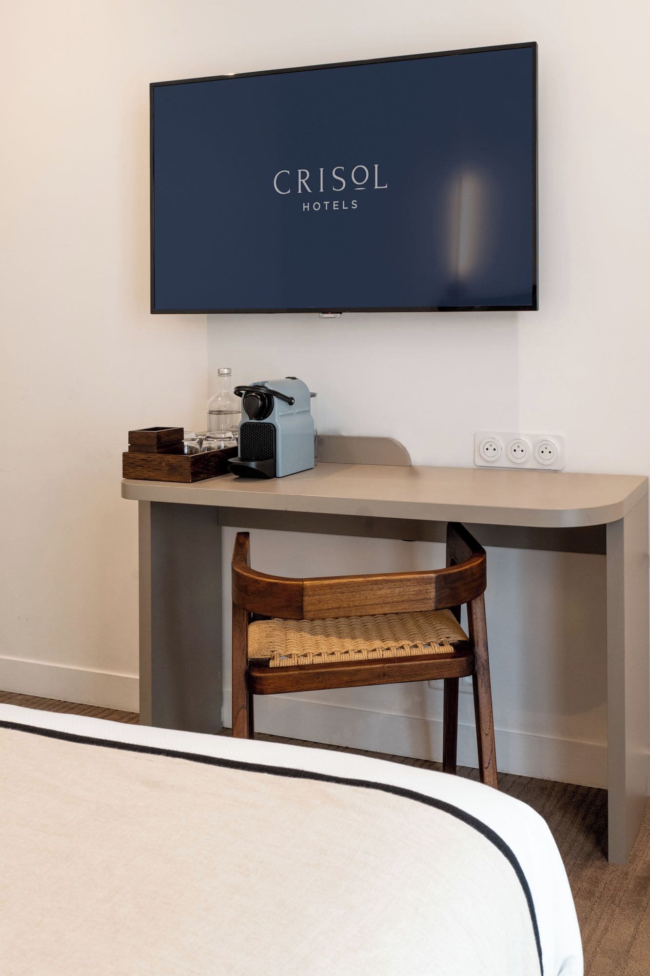 A hotel room with a bed, a desk with a chair, a television, and a power outlet.