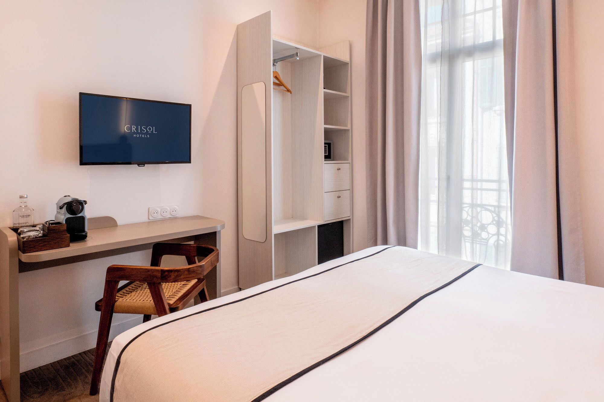 Una camera d'albergo con un letto, una scrivania con sedia, una TV, un armadio e una finestra con tende.