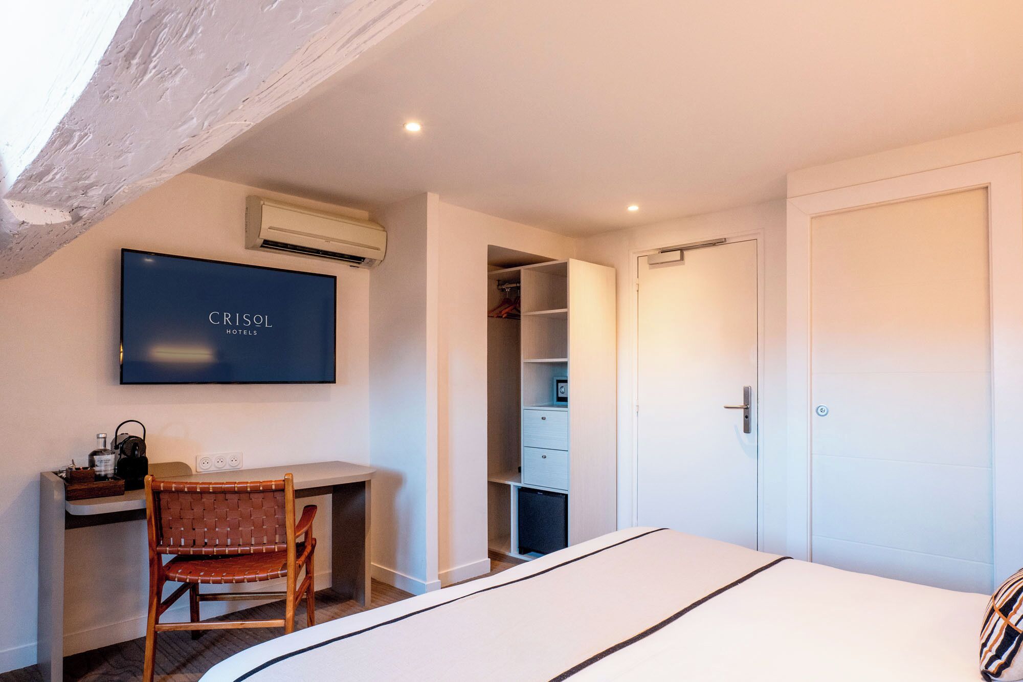Habitación de hotel con cama, escritorio con silla, armario y televisión montada en la pared.
