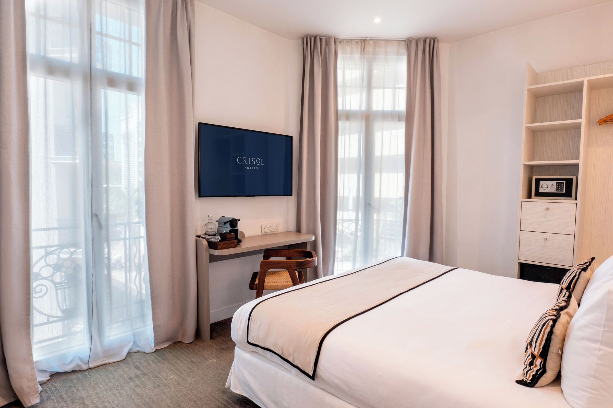 A hotel room with a bed, a desk with a computer, a TV, and a wardrobe.