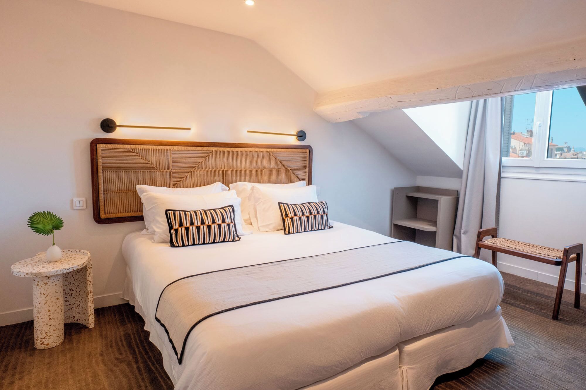 Une chambre avec un grand lit, une petite table de chevet, une chaise et une vue sur la ville par la fenêtre.