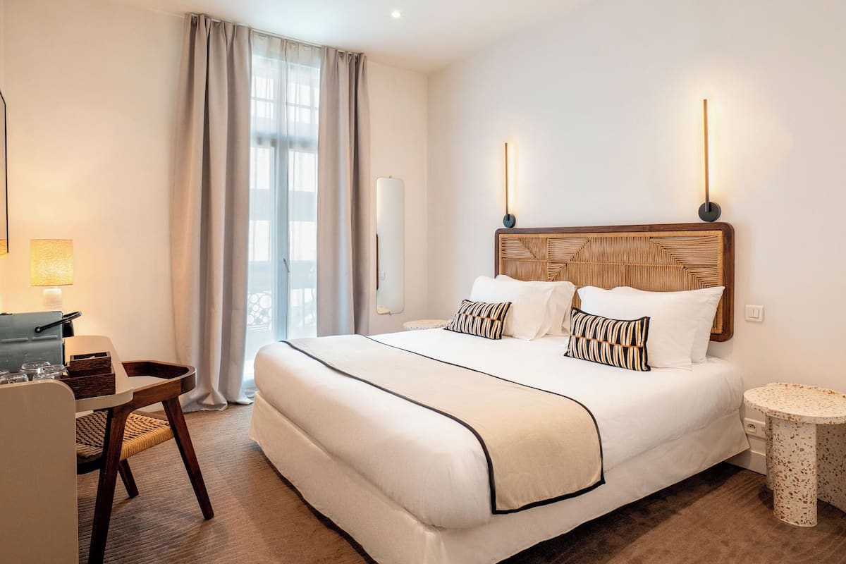 A hotel room with a large bed, a desk, a chair, and a small round table.
