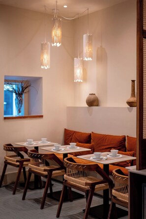 Un coin repas avec des chaises en bois, une table dressée avec de l’assiette blanche et un lustre moderne.