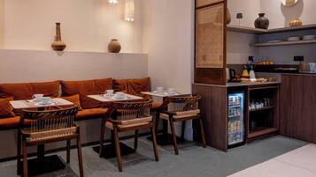 A cozy cafe with a sofa, chairs, a small refrigerator, and a counter with kitchen items.