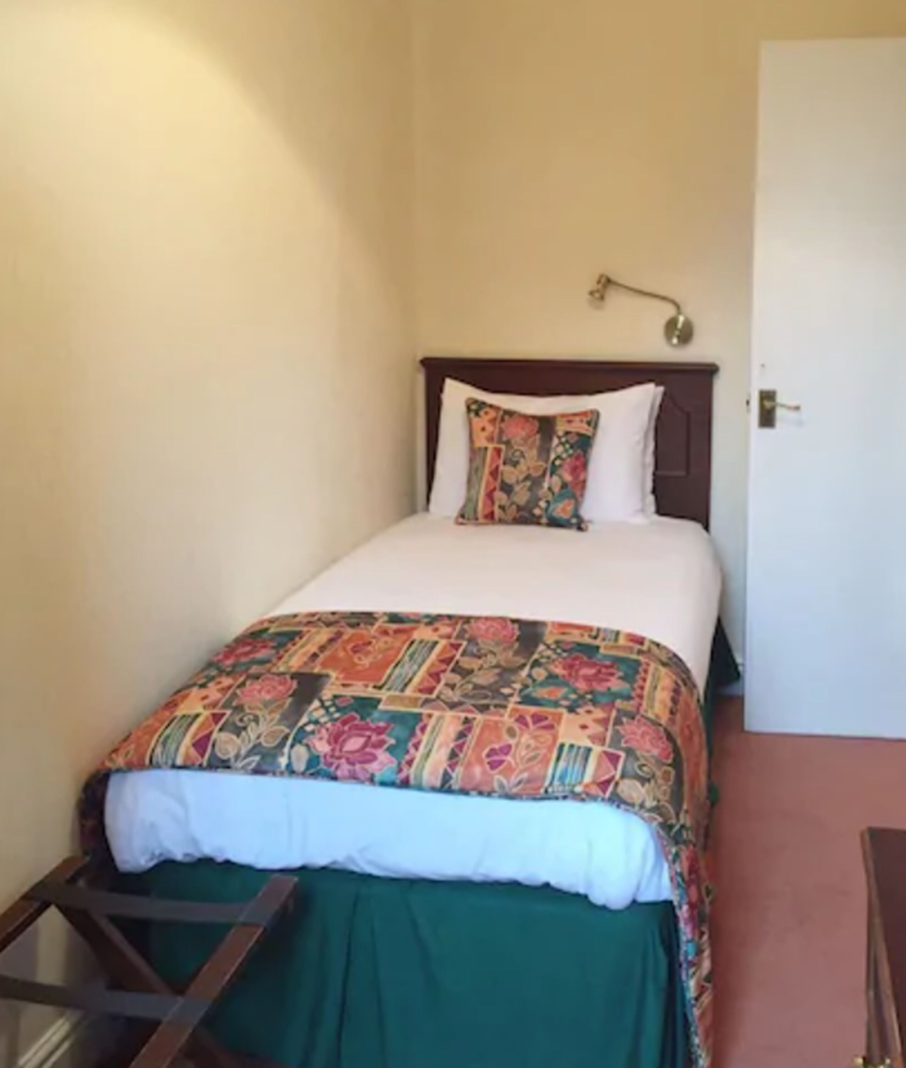 A single bed with a colorful quilt, a wooden headboard, and a bedside lamp.