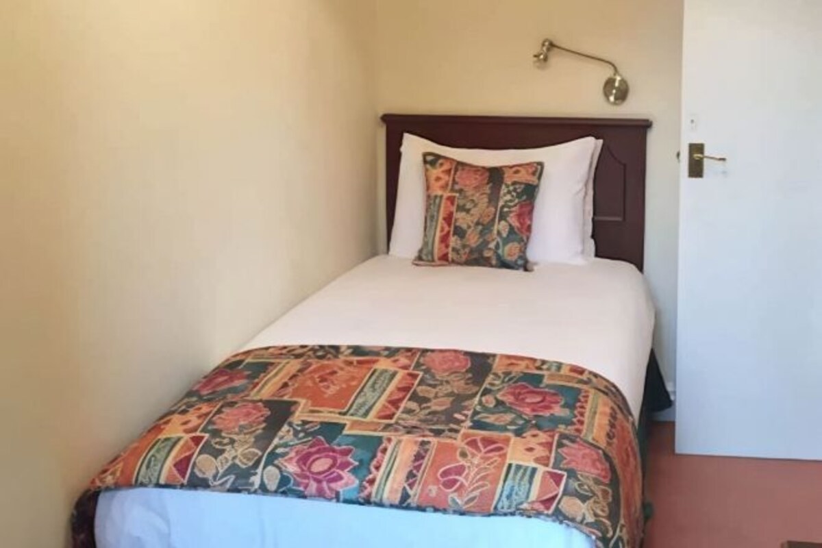 A single bed with a patterned bedspread and two pillows, one with a floral design and the other plain.