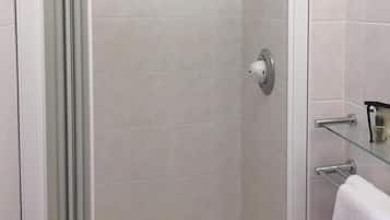 A glass-enclosed shower with a white door, a glass shelf with a towel, and a visible showerhead.