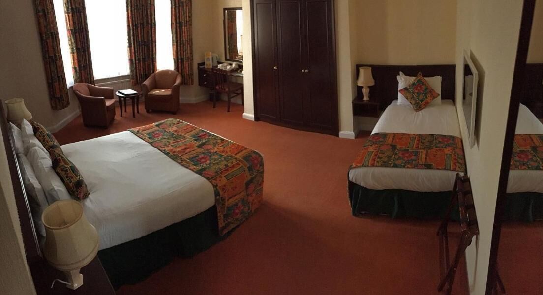 A hotel room with two beds, a desk, a chair, and a wardrobe.