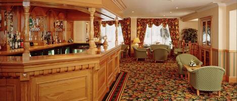 A bar area with wooden bar counter and stools, a patterned carpet, and a seating area with chairs and a table.