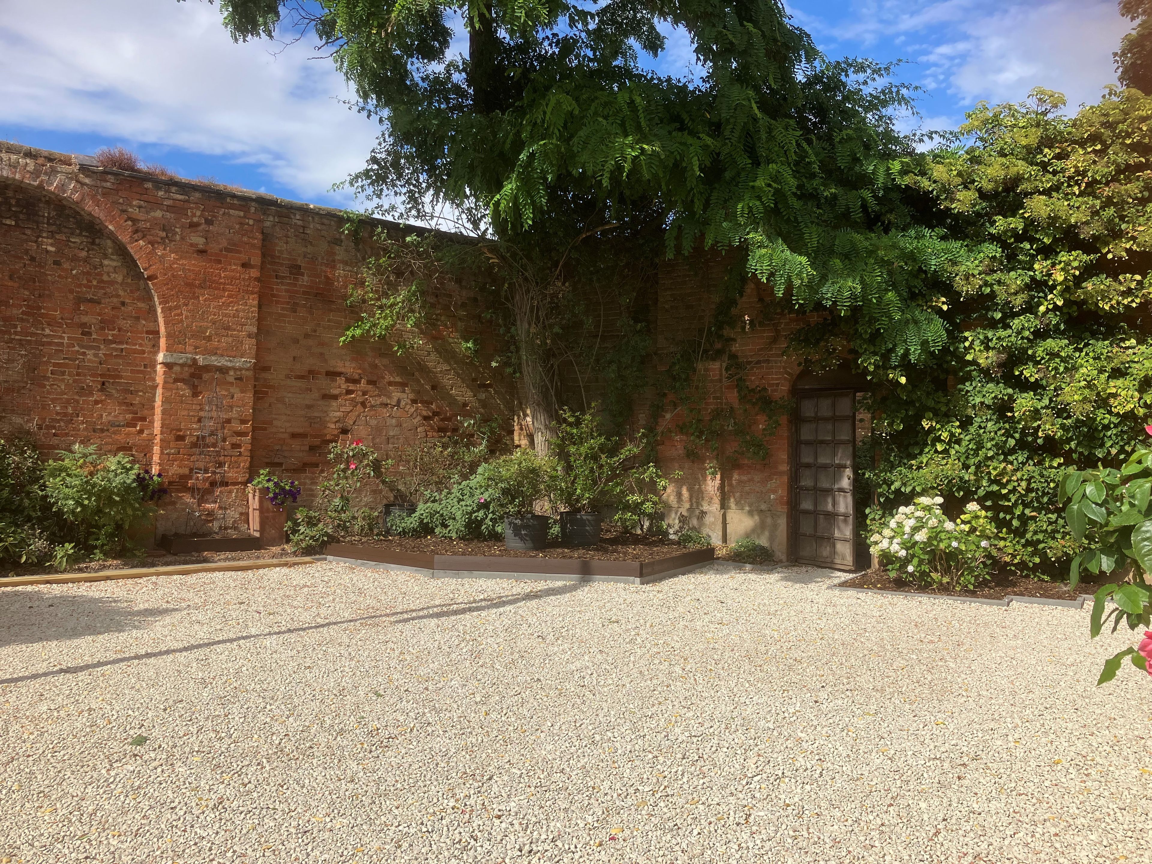 A courtyard with a gravel ground, a brick wall, and a wooden door.