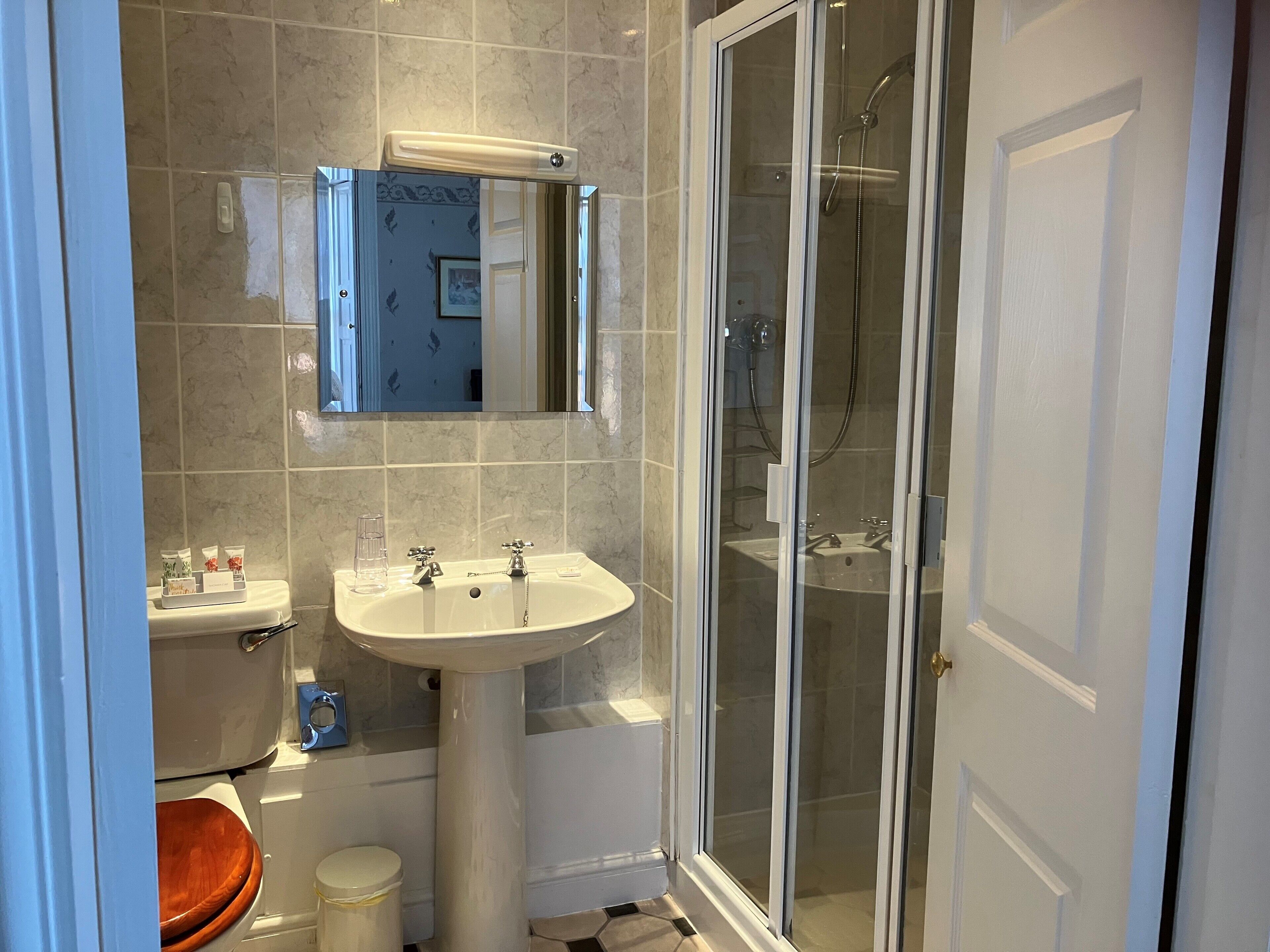 Un baño con inodoro, lavabo, espejo, ducha y cabina de ducha acristalada.
