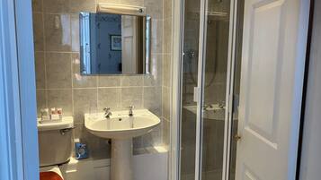 Un baño con inodoro, lavabo, espejo, ducha y cabina de ducha acristalada.