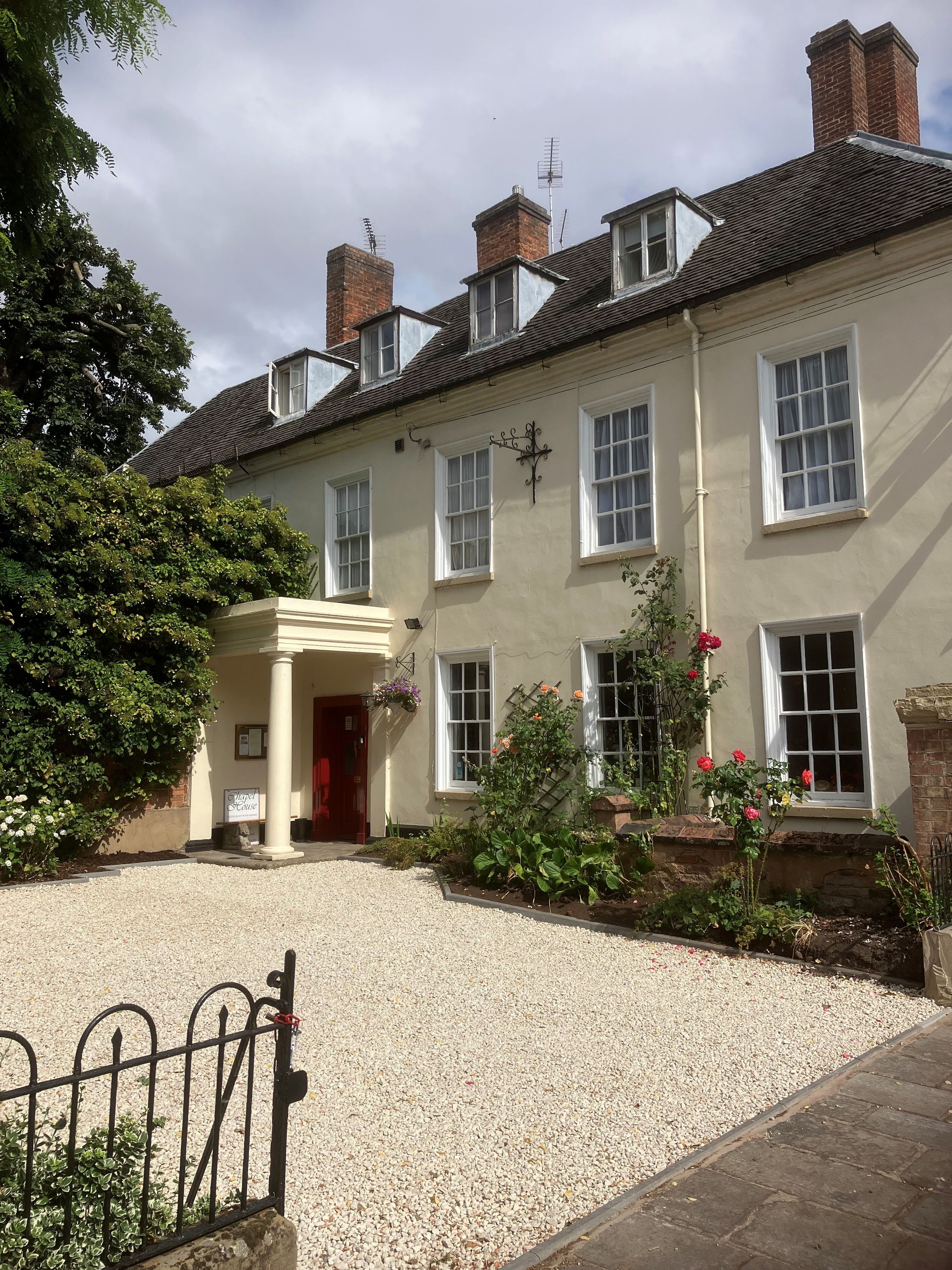 A traditional building with a gravel driveway, a gated entrance, and a flower bed with red flowers.