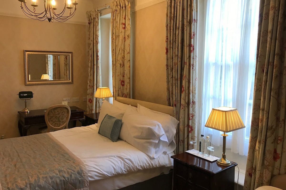 Une chambre d’hôtel avec un lit, une table de chevet avec une lampe, un miroir et des rideaux.