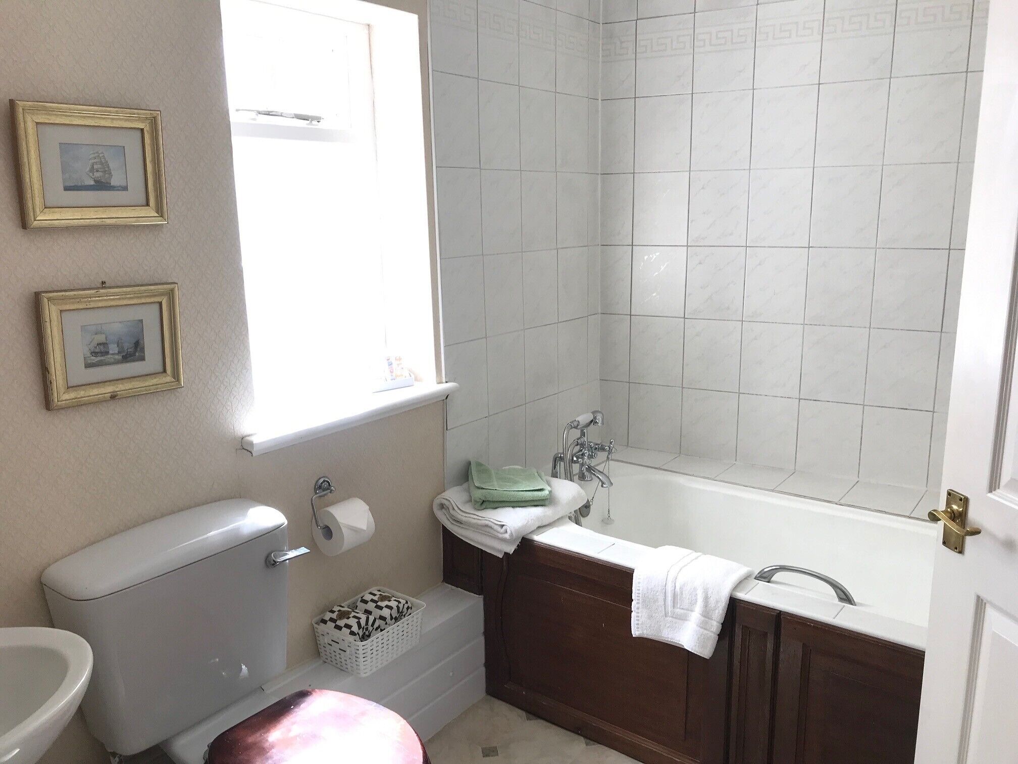 A bathroom with a toilet, sink, bathtub, and two framed pictures on the wall.