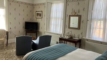Habitación de hotel con cama, dos sillones, escritorio con televisor y ventana con cortinas.