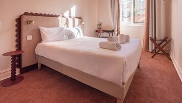 Una cama bien hecha con ropa blanca, un cabecero de madera y una mesita de noche con un jarrón de flores.