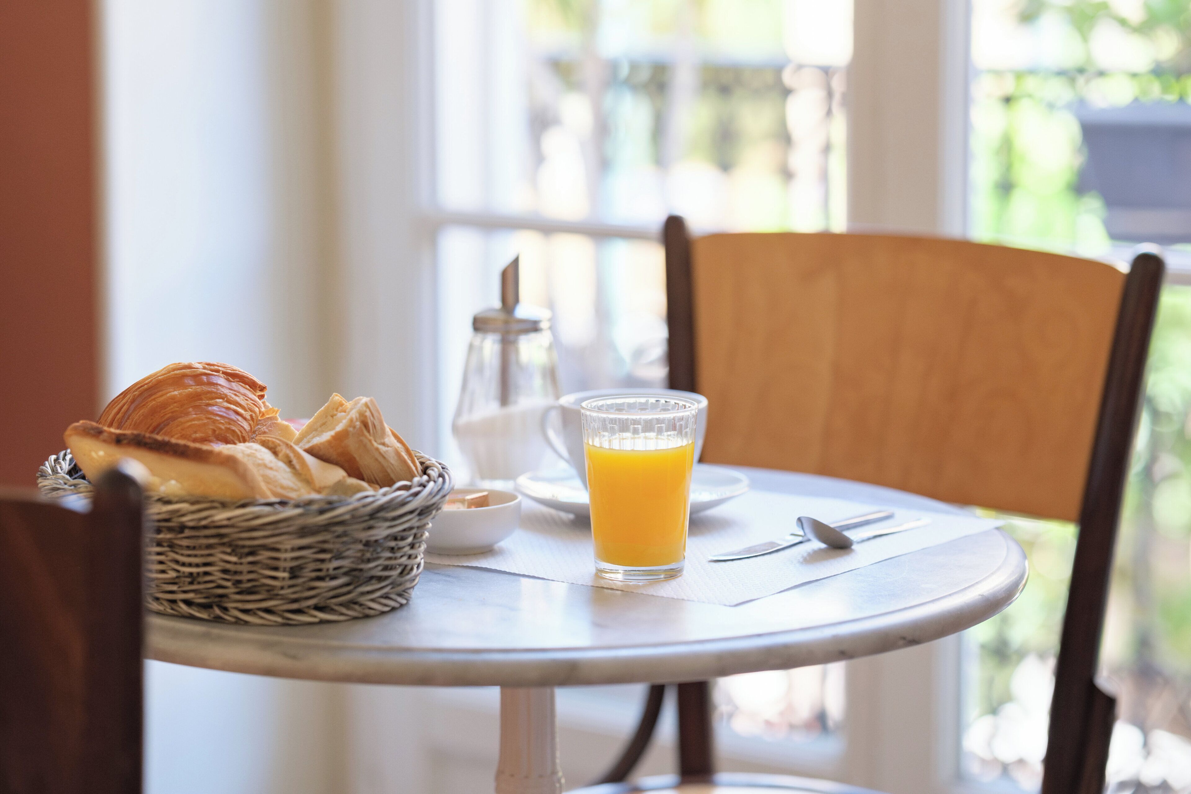 Una mesa con croissants, un vaso de jugo de naranja y un dispensador de azúcar.
