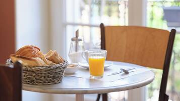 Una mesa con croissants, un vaso de jugo de naranja y un dispensador de azúcar.