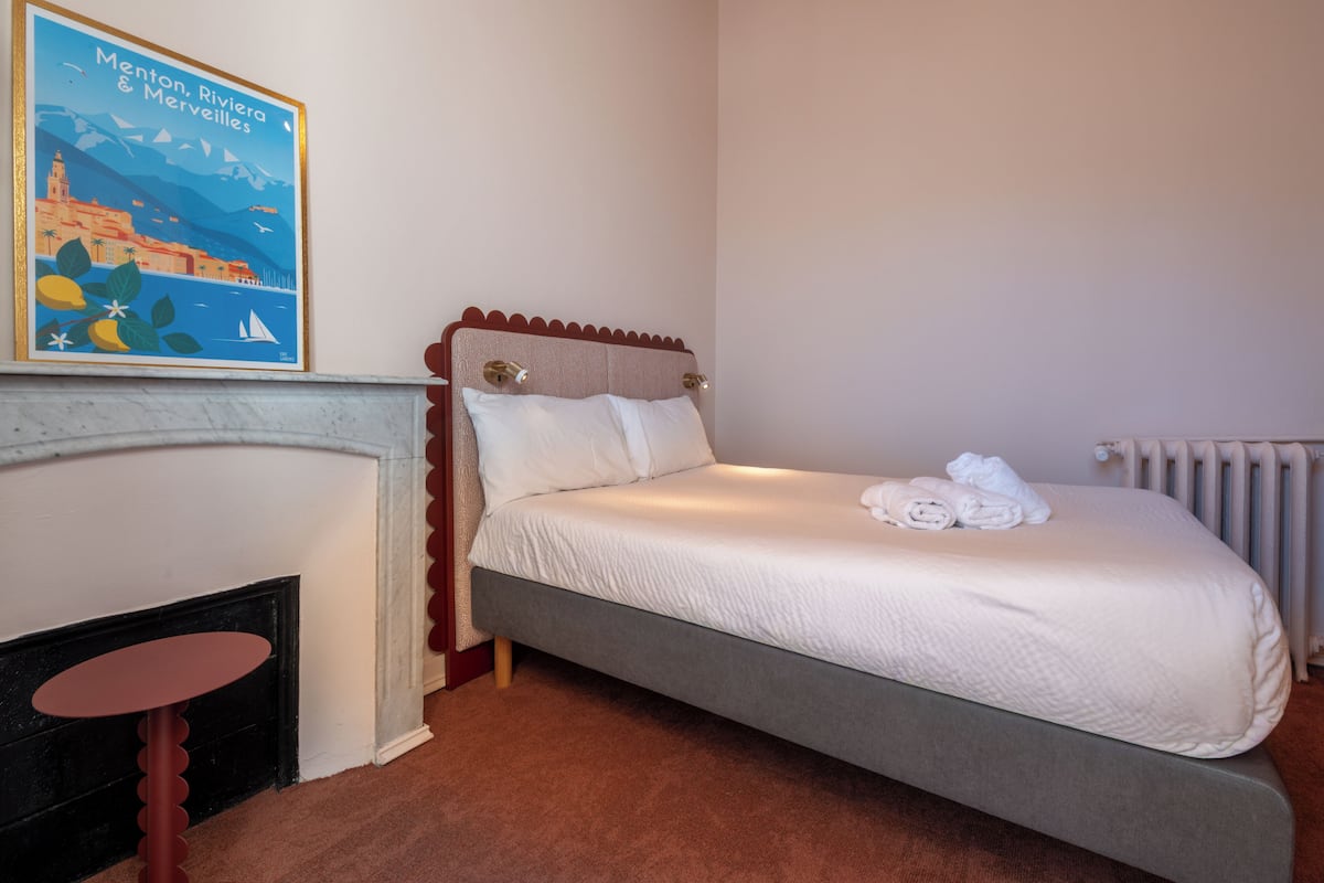 A bedroom with a bed, a fireplace, and a painting on the wall.