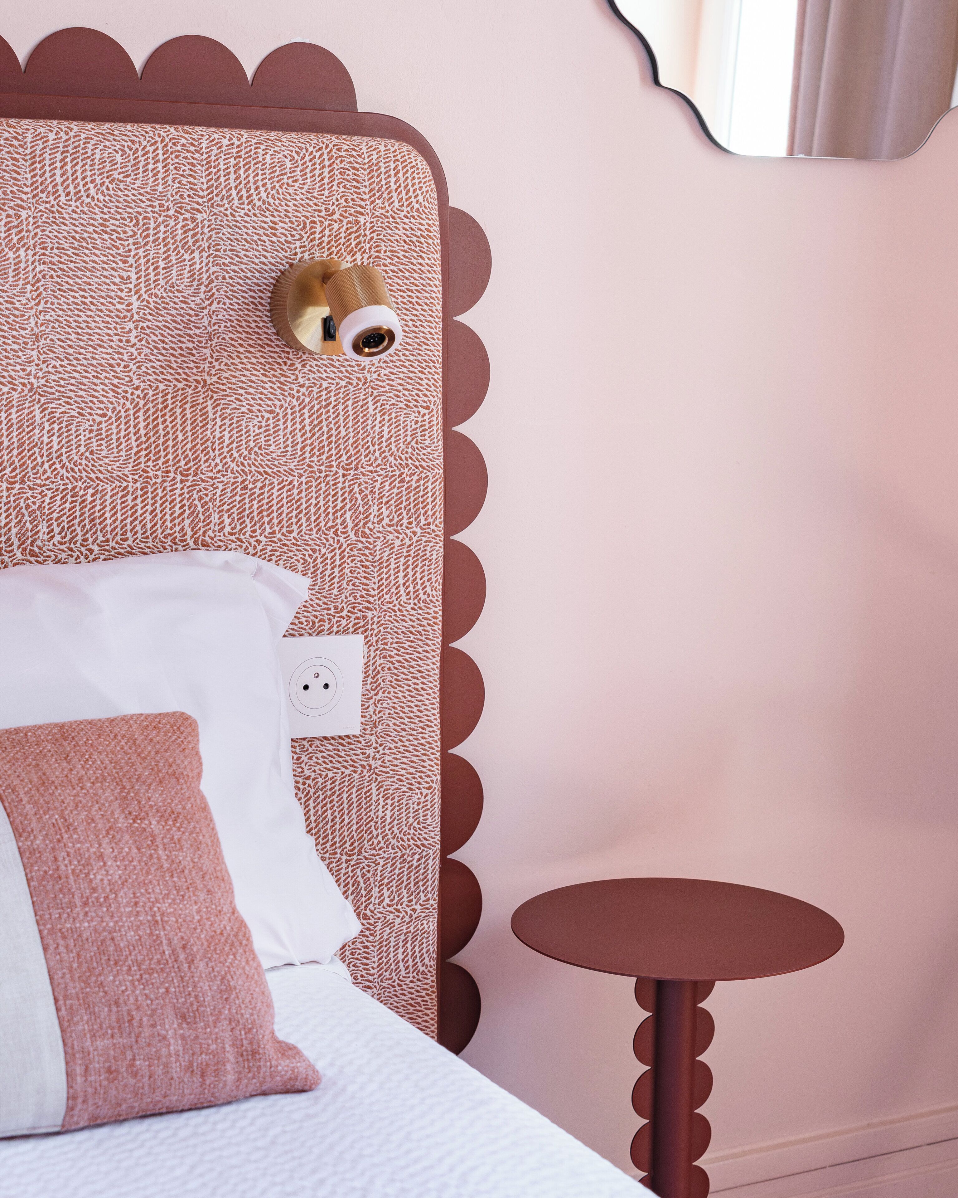 A bed with a textured headboard, a bedside table, and a power outlet.