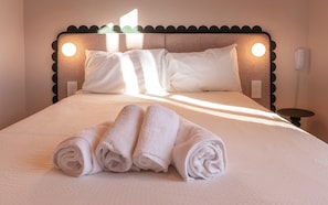 A neatly made bed with rolled towels, a textured headboard, and bedside lamps.
