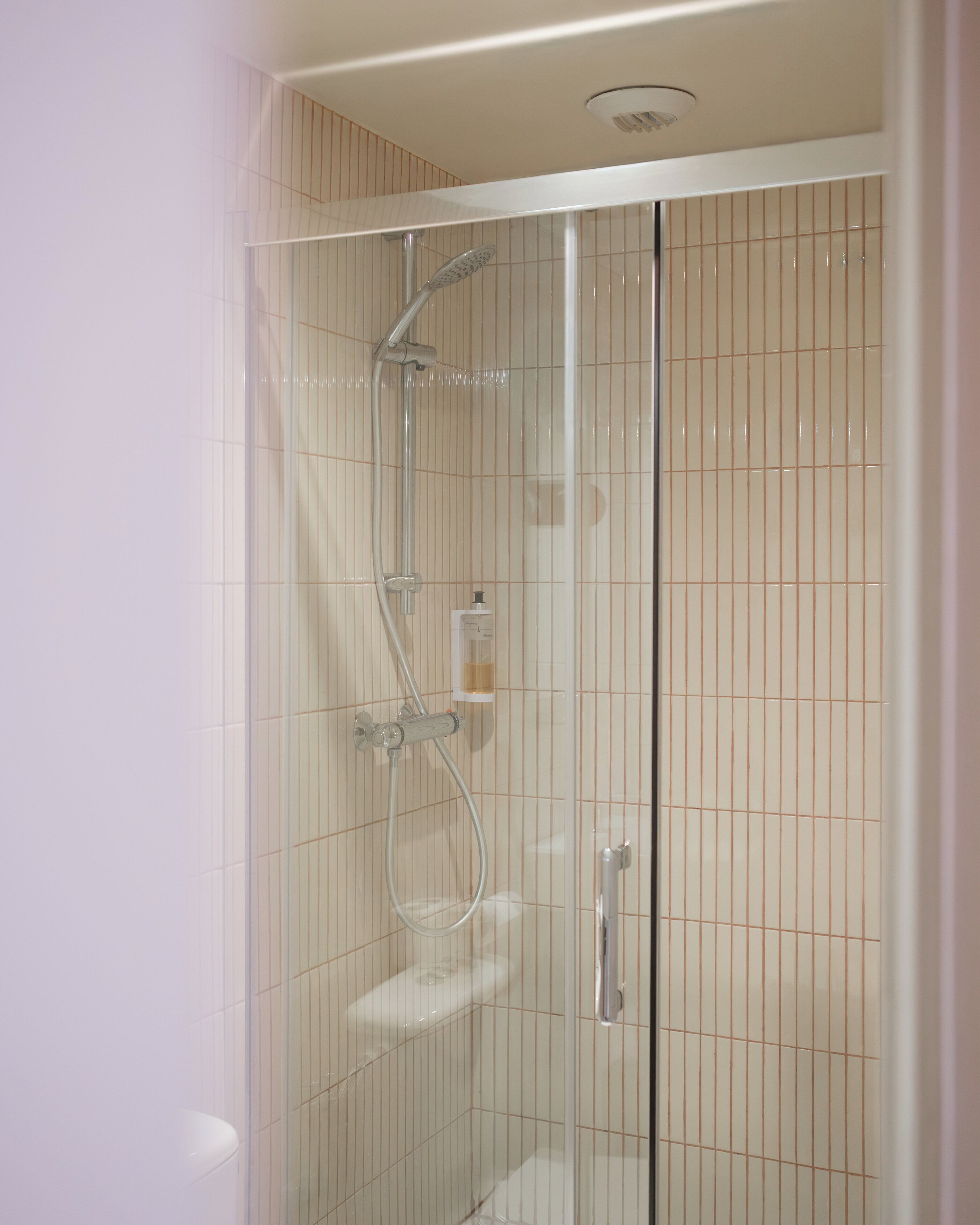 Une cabine de douche fermée par des parois en verre, dotée d’un pommeau de douche à main et d’un robinet fixé au mur.