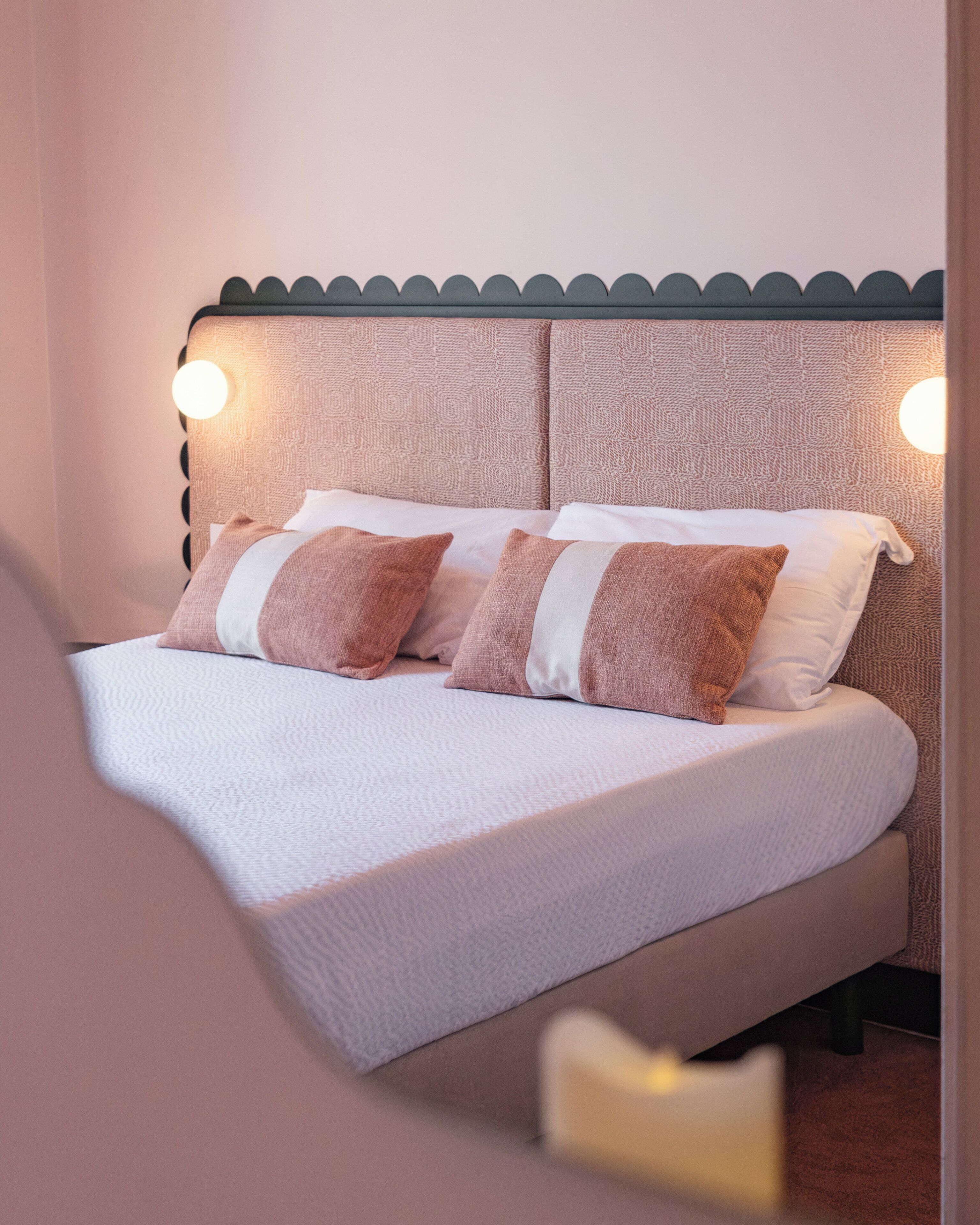 Een bed met een gestructureerd hoofdeinde, twee kussens en een nachtkastje met een lamp.