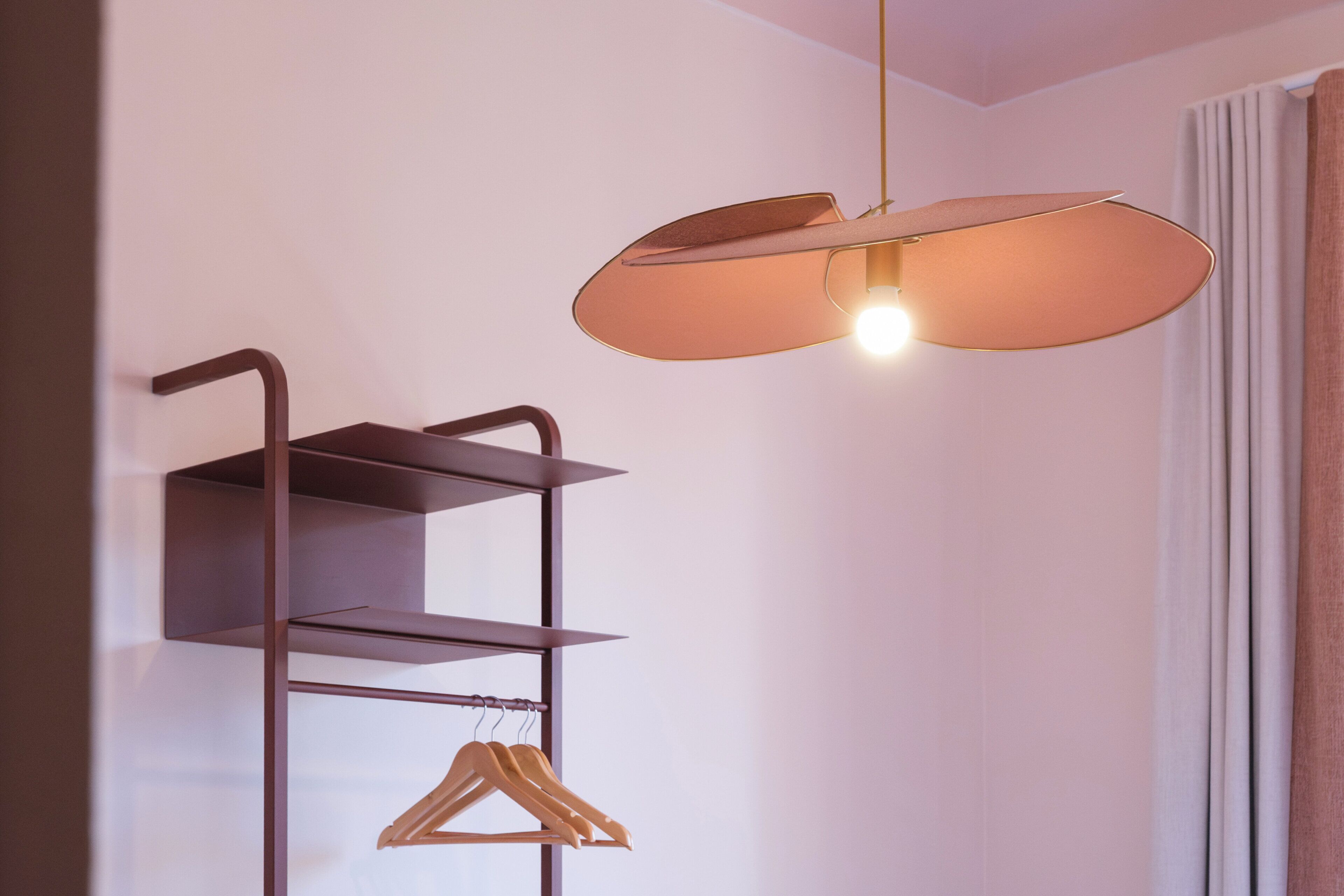A room with a wall-mounted metal shelf unit with a single hanger and a pendant light fixture.