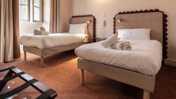 Habitación de hotel con dos camas, cabecero de madera, mesita de noche y ventana con cortinas.
