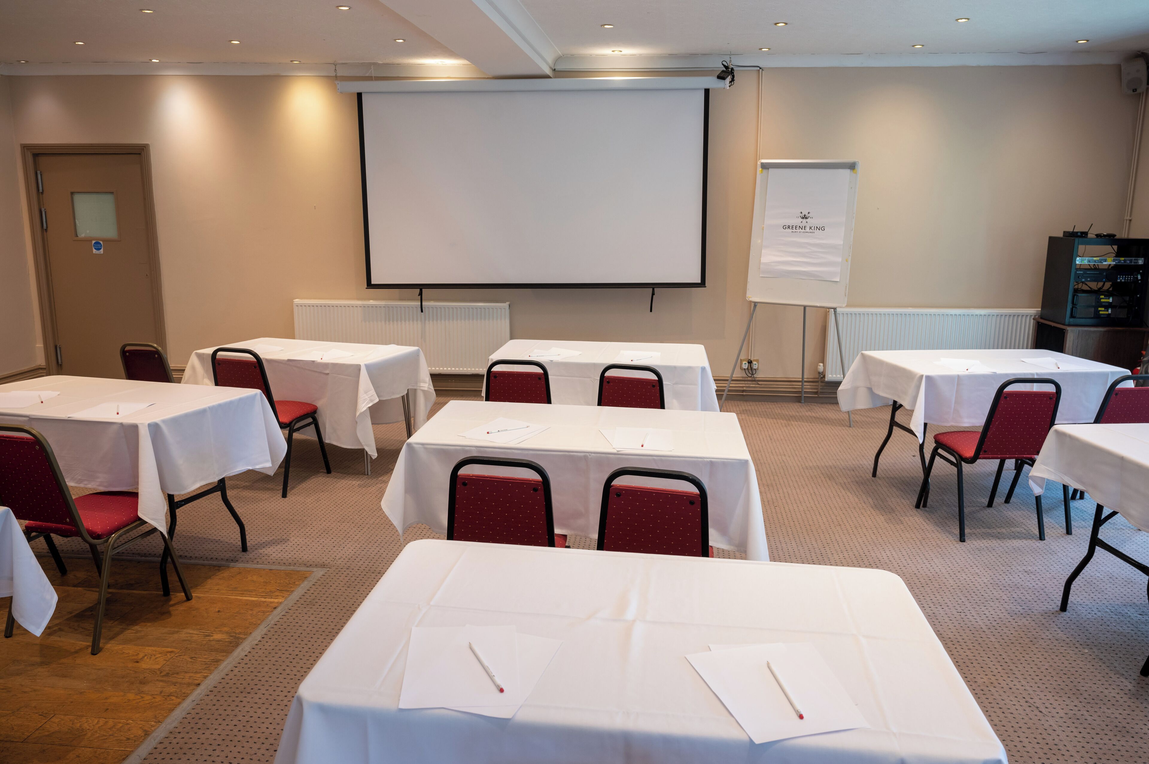 A conference room with multiple tables and chairs, a projector screen, and a whiteboard.