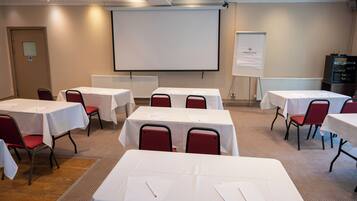 A conference room with multiple tables and chairs, a projector screen, and a whiteboard.