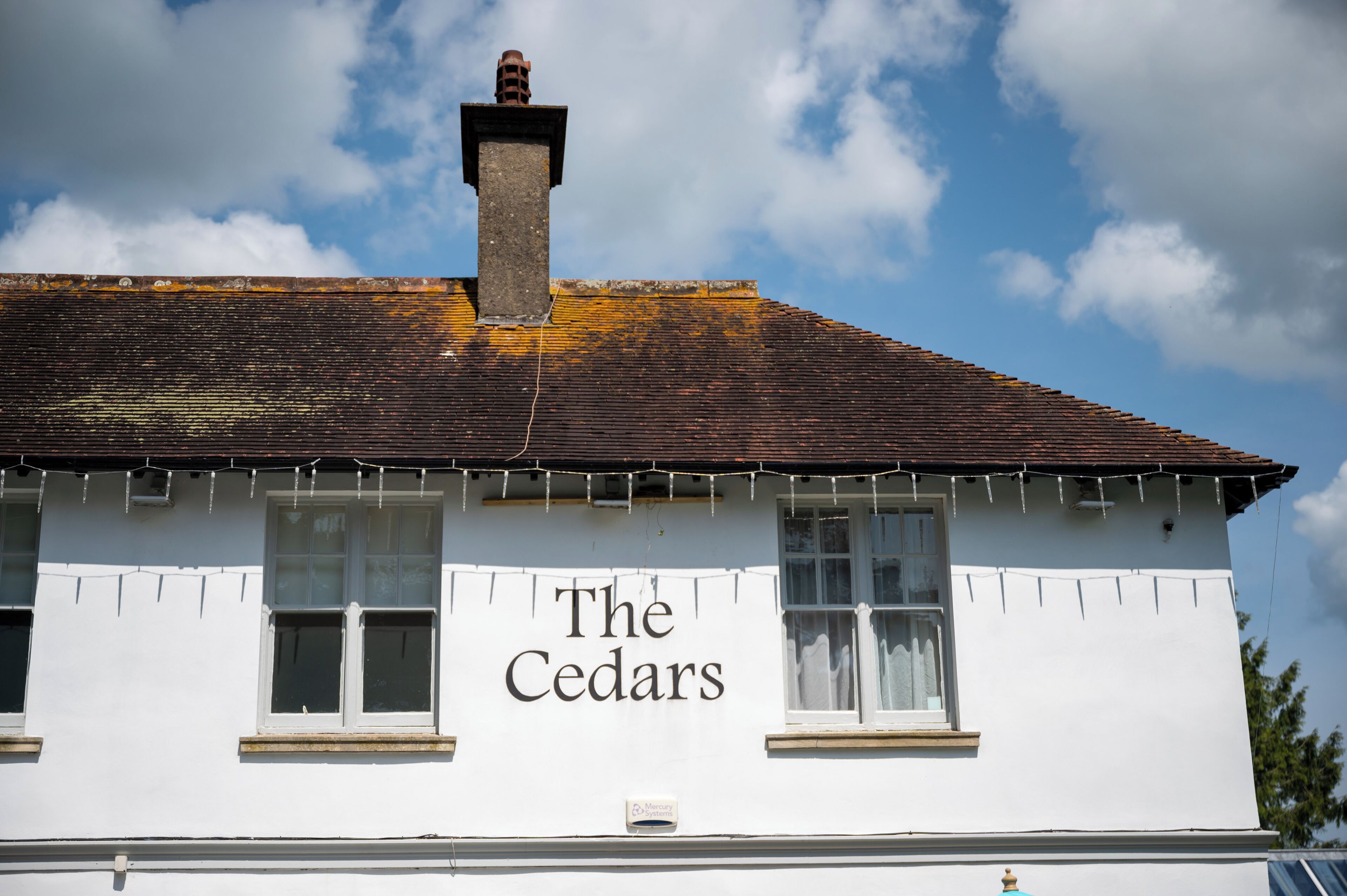 A building with the sign "The Cedars" on its facade, featuring a traditional design with a pitched roof and multiple windows.
