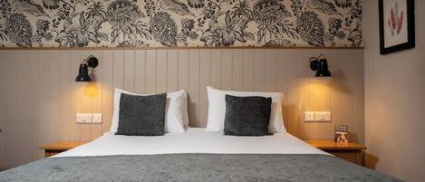A hotel room with a large bed, two bedside lamps, a floral-patterned wallpaper, and a framed artwork on the wall.