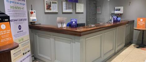 A hotel reception area with a check-in counter, a sign indicating a takeaway collection point, and a sign for hotel guests to check in.