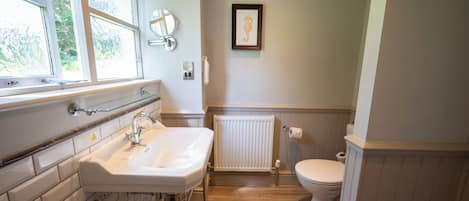 A bathroom with a white sink, a toilet, a framed seahorse artwork, and a window with a view of greenery.