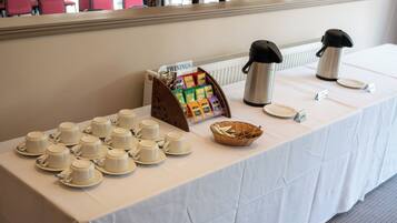 A breakfast buffet setup with multiple cups, a coffee pot, and a basket of bread.