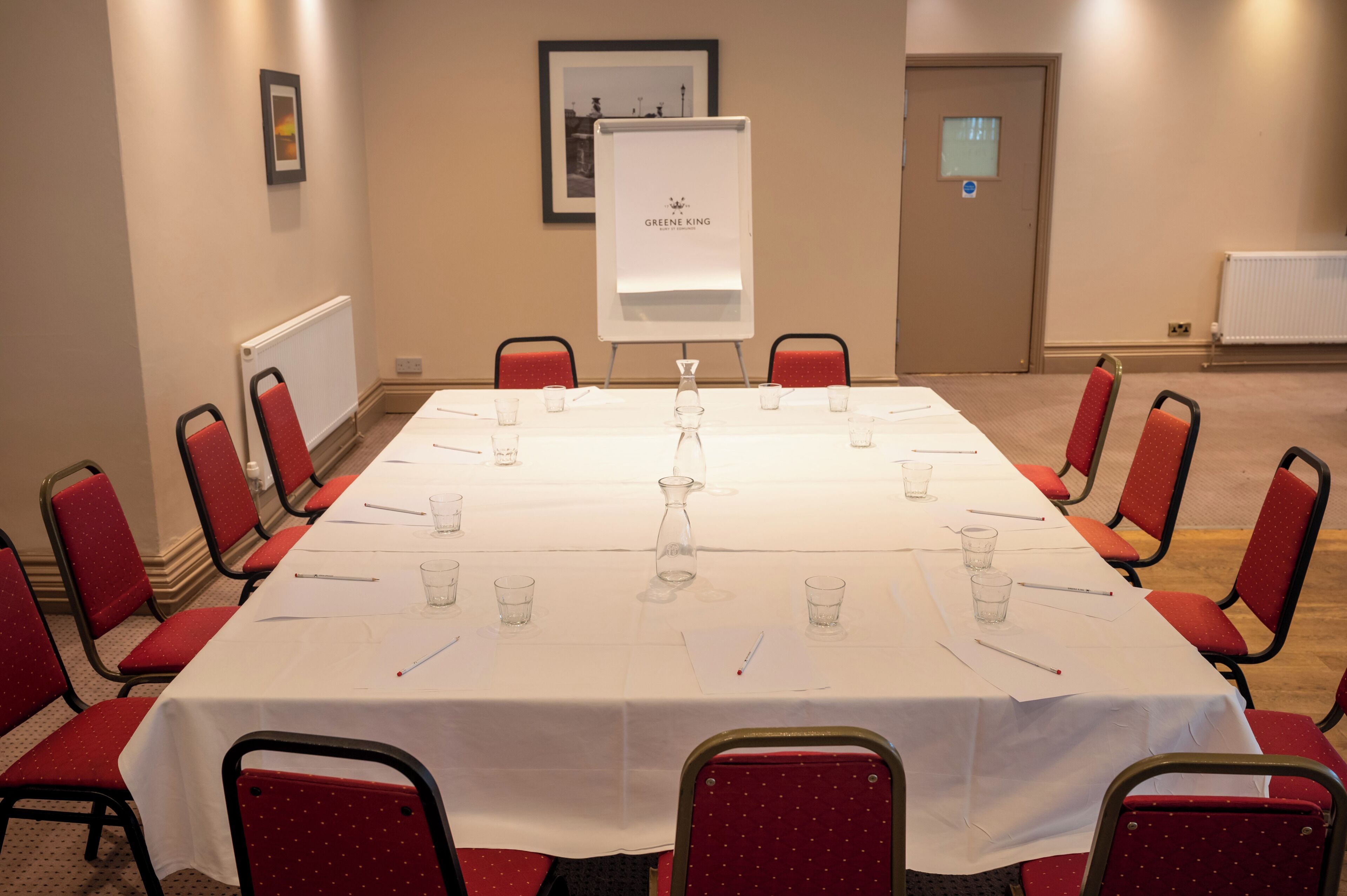 A conference room with a long table, red chairs, a whiteboard, and a framed picture on the wall.