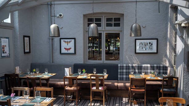 A restaurant with wooden tables and chairs, a bench, and framed pictures on the walls. - The Cedars Inn by Greene King Inns (Barnstaple)