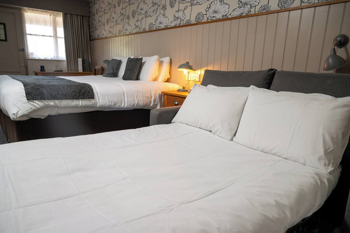 Ein Hotelzimmer mit zwei Betten, einem Nachttisch mit Lampe und einem Fenster mit Vorhängen.